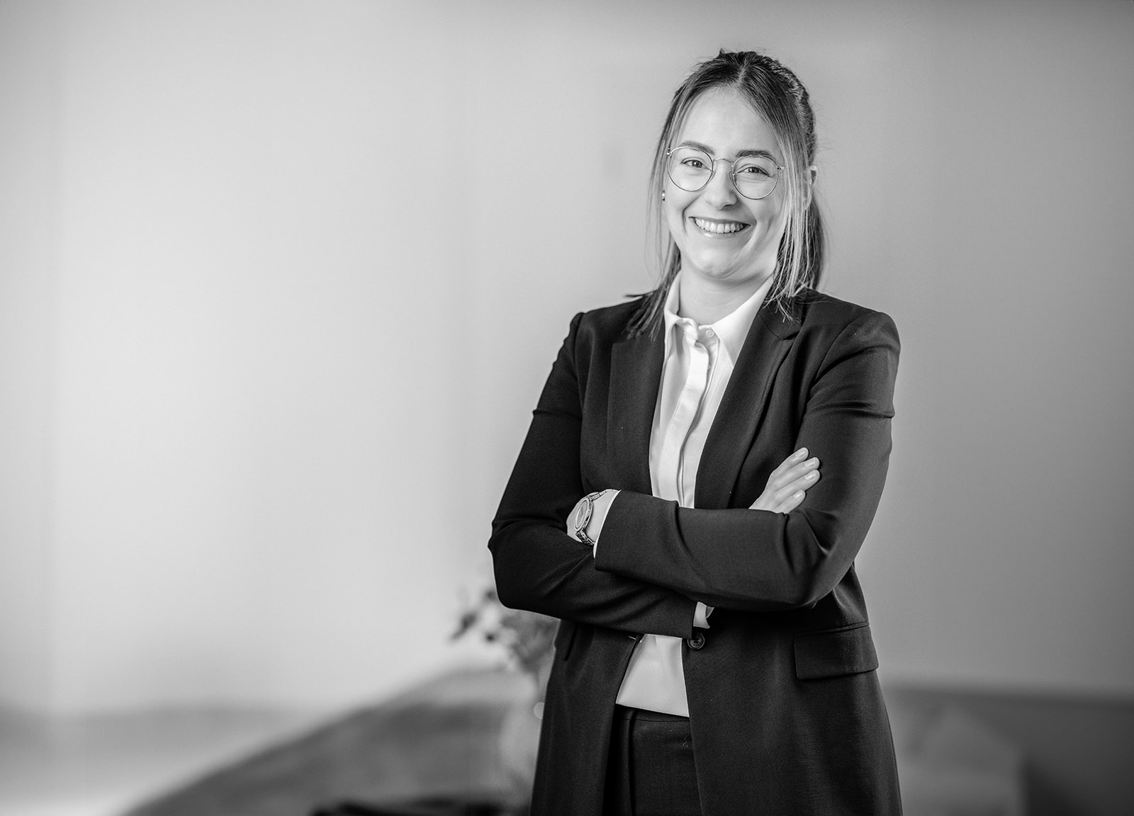 Business Portrait Fotograf Ahaus: Frau im Anzug mit verschränkten Armen und Lächeln schwarz weiß fotografiert.
